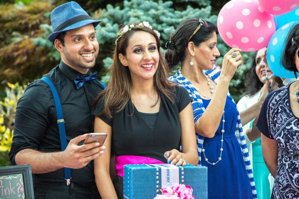 well-dressed husband with hat smiles with his wife during gender reveal party