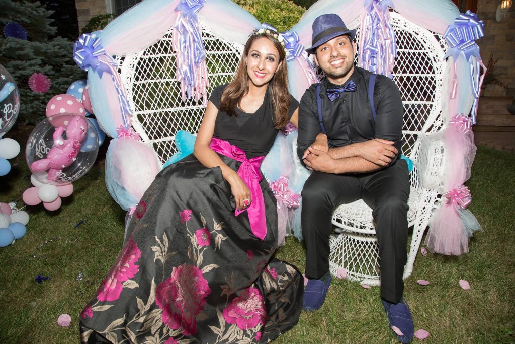 couple posing in large white whicker chairs during a gender reveal party